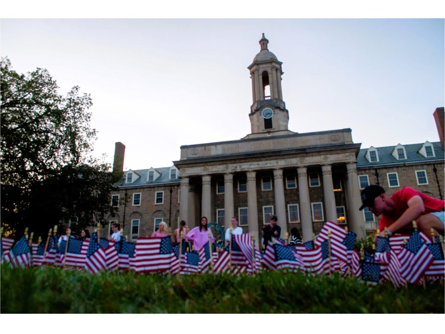 Students place American flags in the grass in front of a campus building