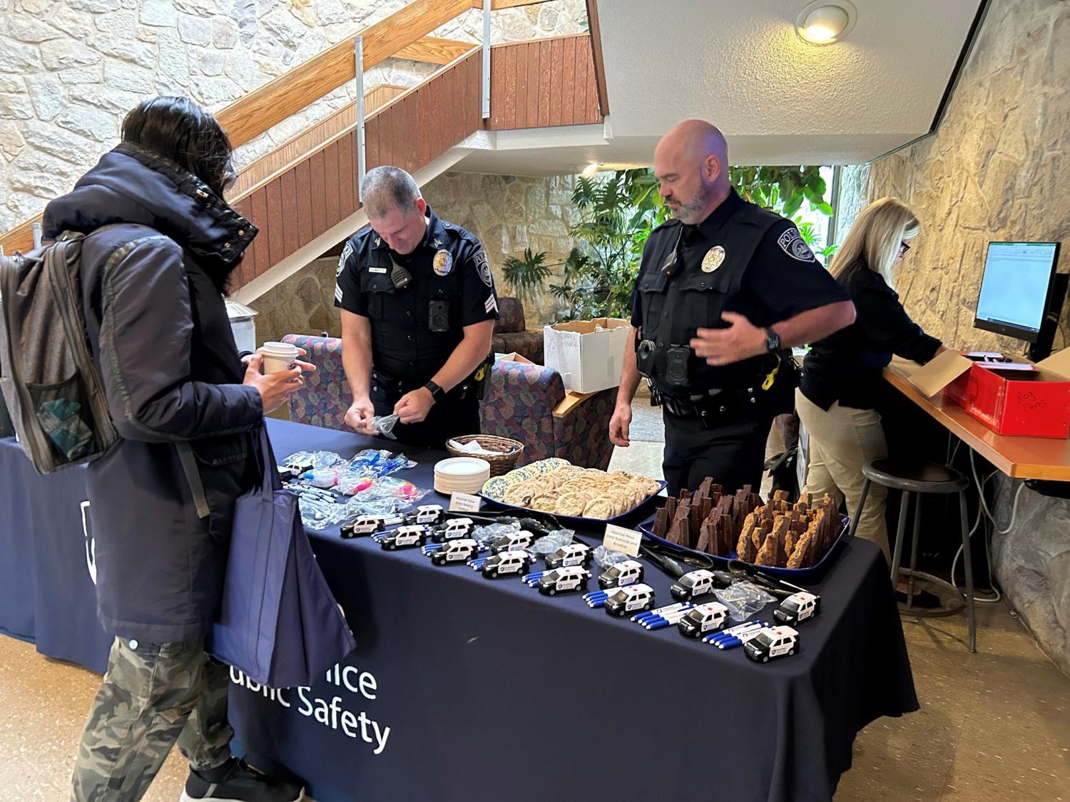 Two officers interact with student at table with coffee, pastries and information
