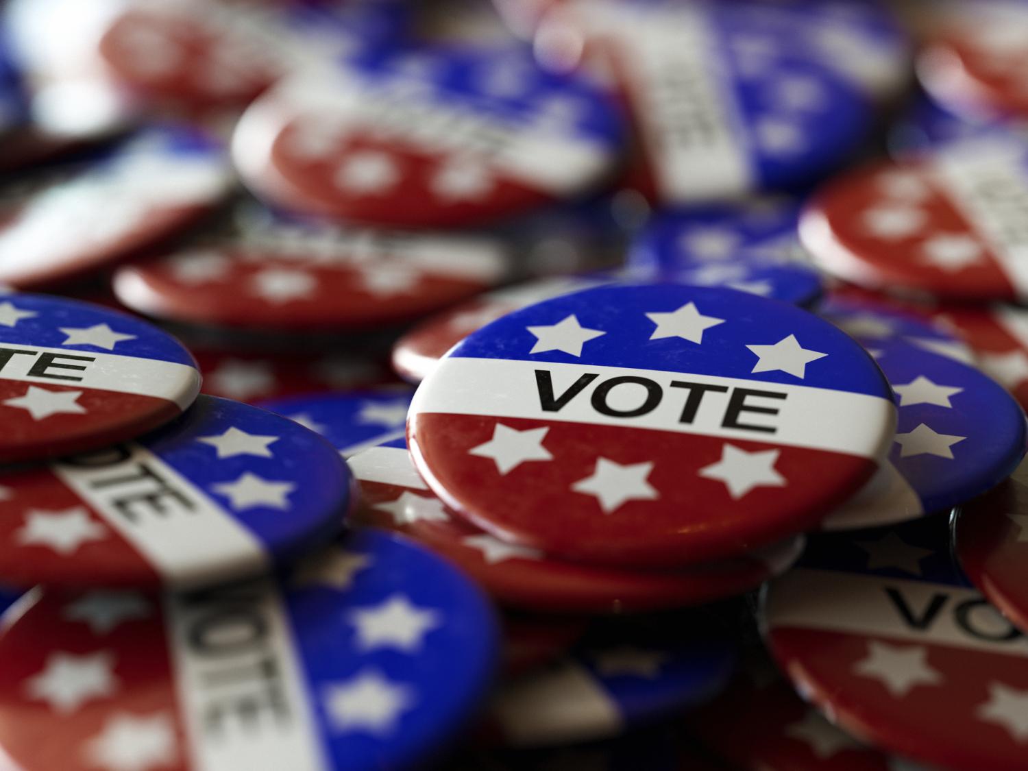 A pile of pins in red, white and blue with six white stars and a white stripe that reads "VOTE"