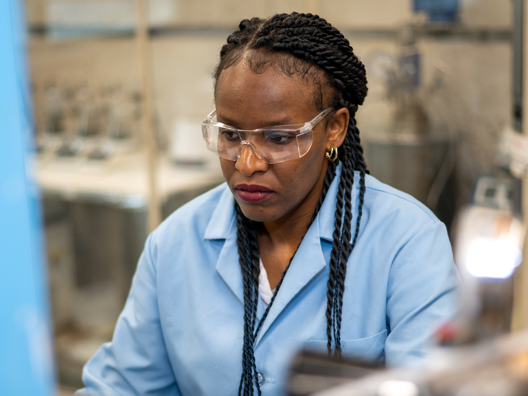 Melissa Gonte wearing a blue lab coat and safety glasses in a lab. 