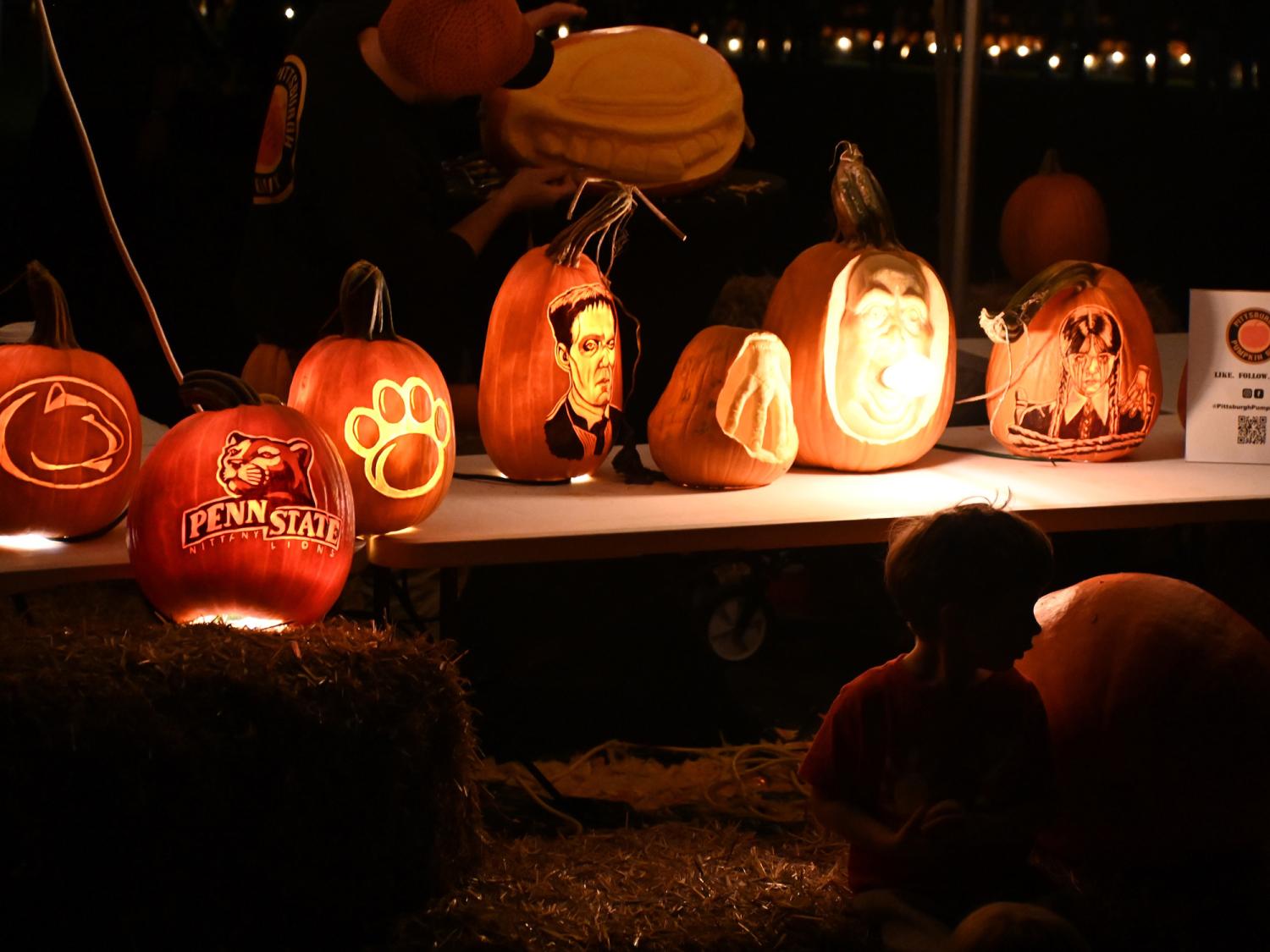 A lineup of carved pumpkins at night at Pumpkin Fest in The Arboretum at Penn State.