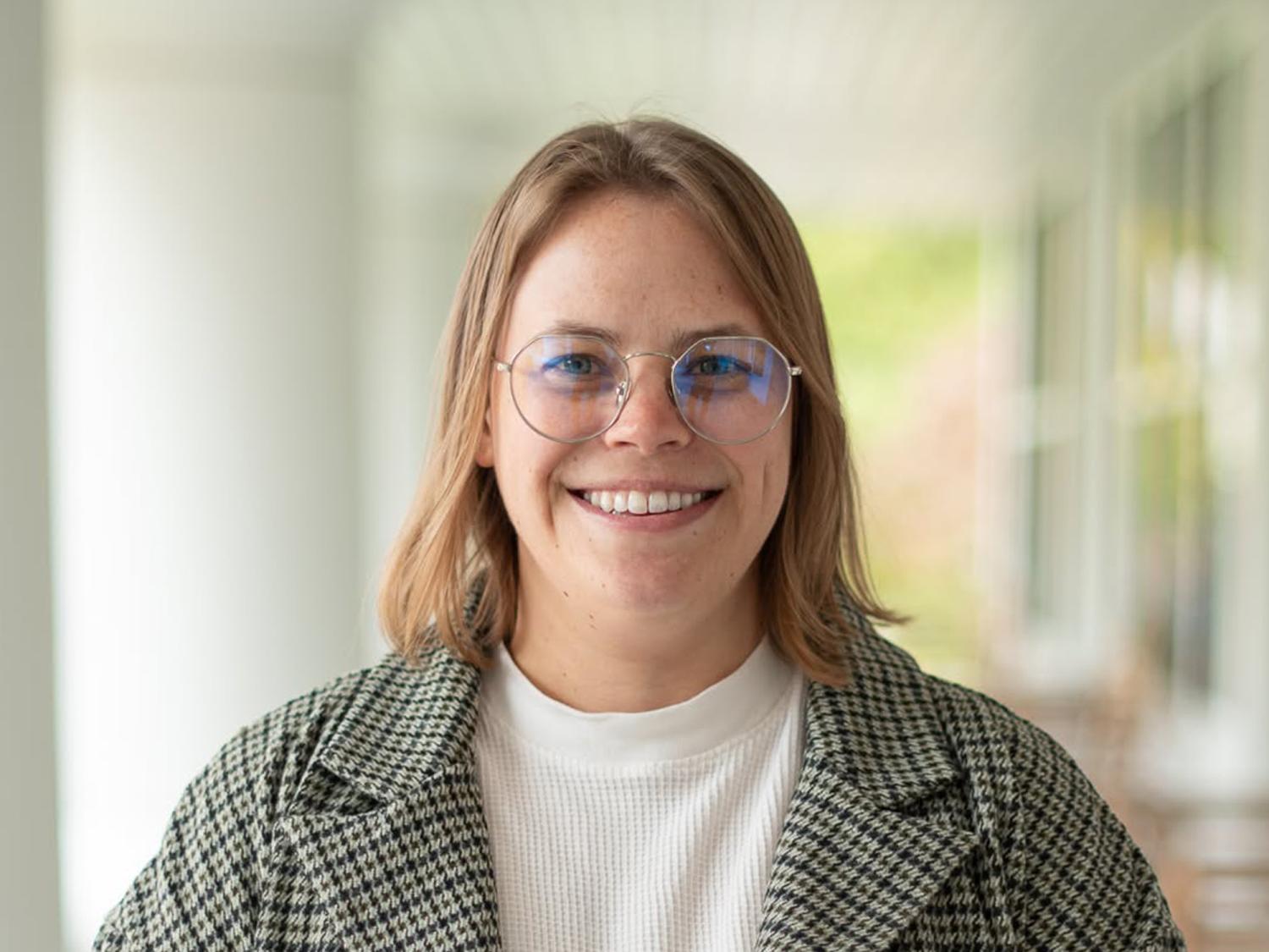 A woman with shoulder-length dark blond hair and glasses smiling.