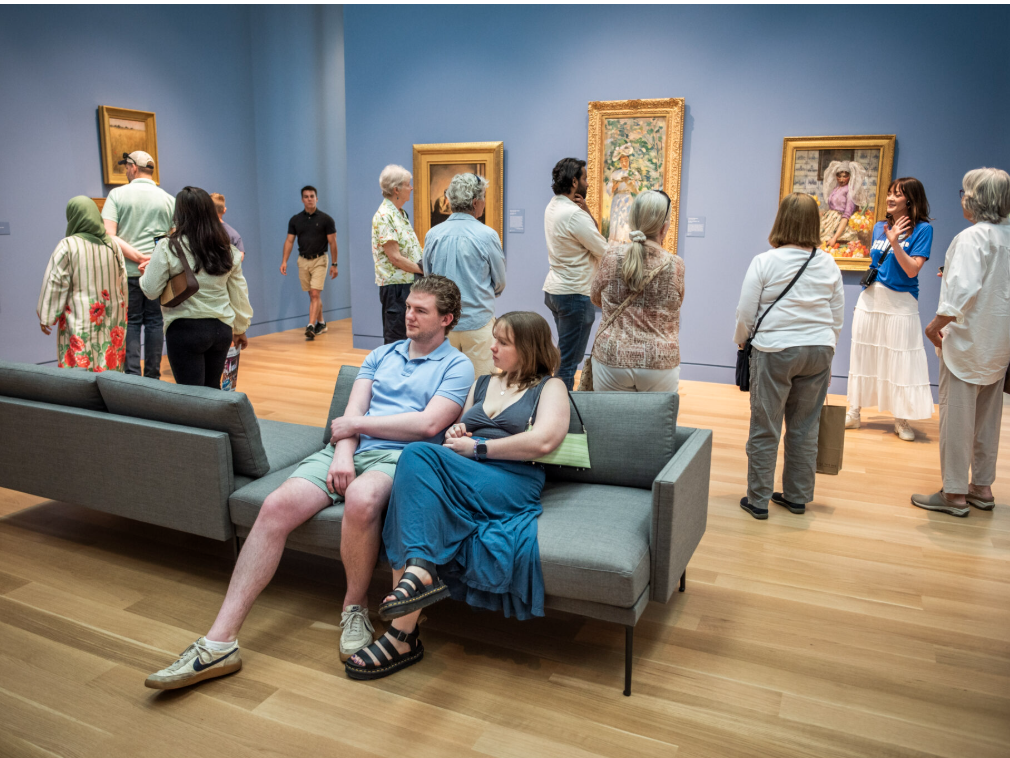 People sitting and walking through a museum with paintings on the blue walls