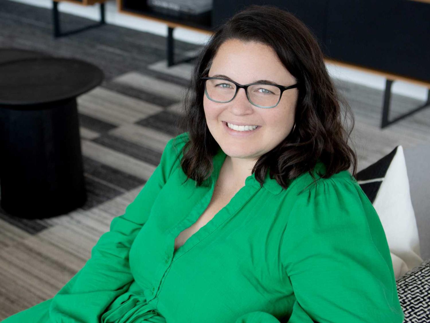 A photo of a smiling Liz Minne, who smiling while sitting and wearing glasses