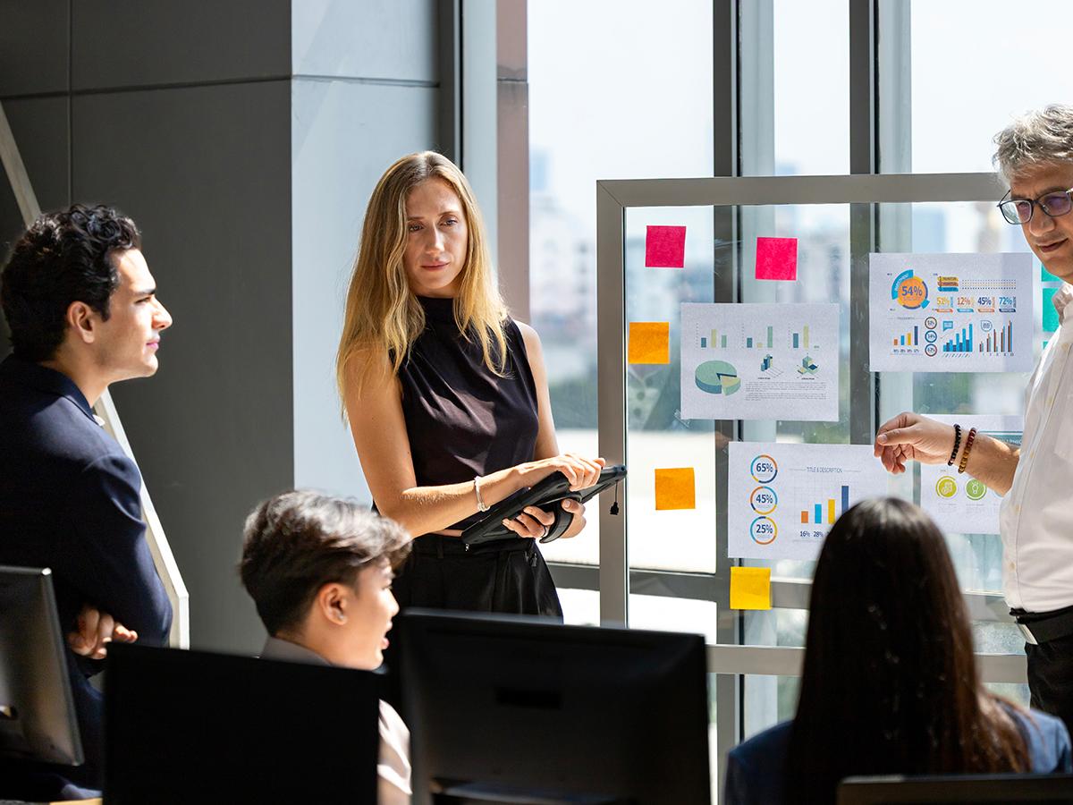 Business team reviews charts and graphs on a presentation board in a bright office.