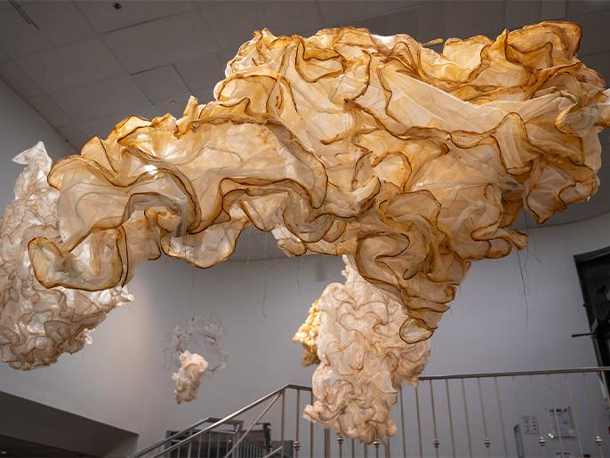 An image of a large artwork resembling tan crinkled fabric hanging from the ceiling of an art gallery