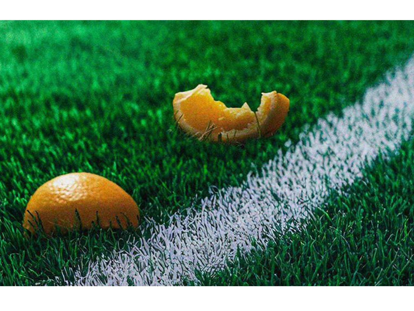Image of a close-up shot of a soccer field three orange peels laying on the ground
