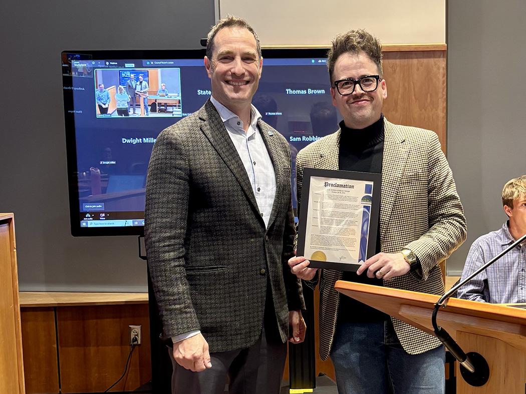 Two men standing side by side with one holding a framed document.
