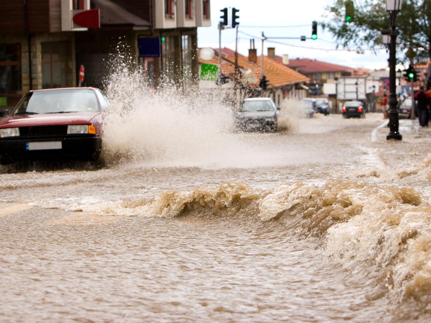 A car driving through a flooded street is nearly overtaken by a swell in water