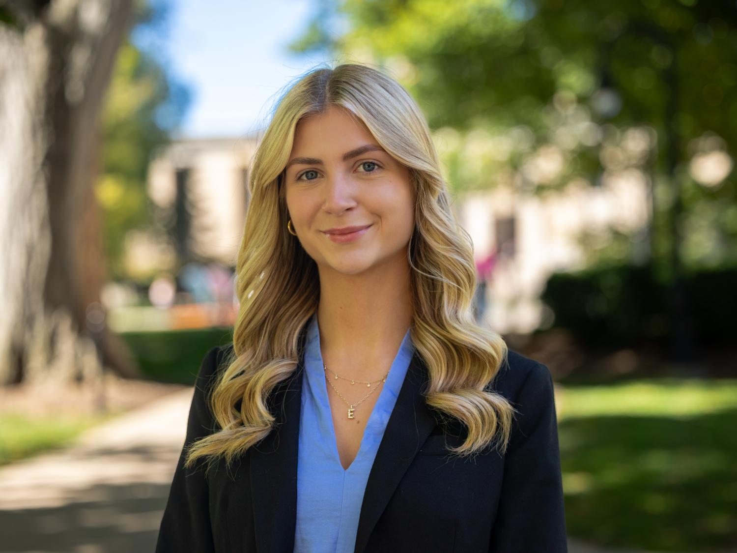 Erin Gregorian wears a black blazer over a blue shirt while standing outdoors.