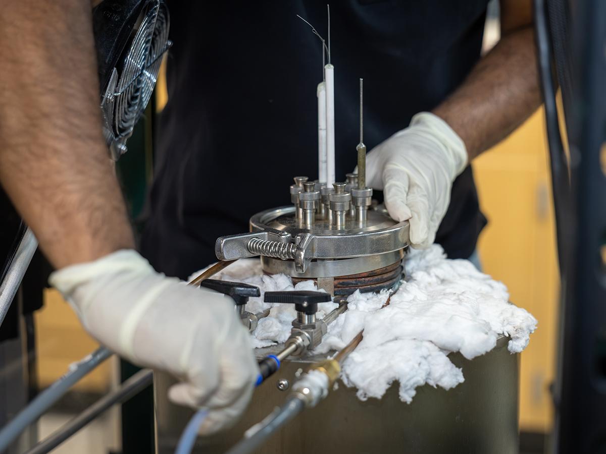 A person wearing gloves closes the lid of a small reaction chamber in a lab. 