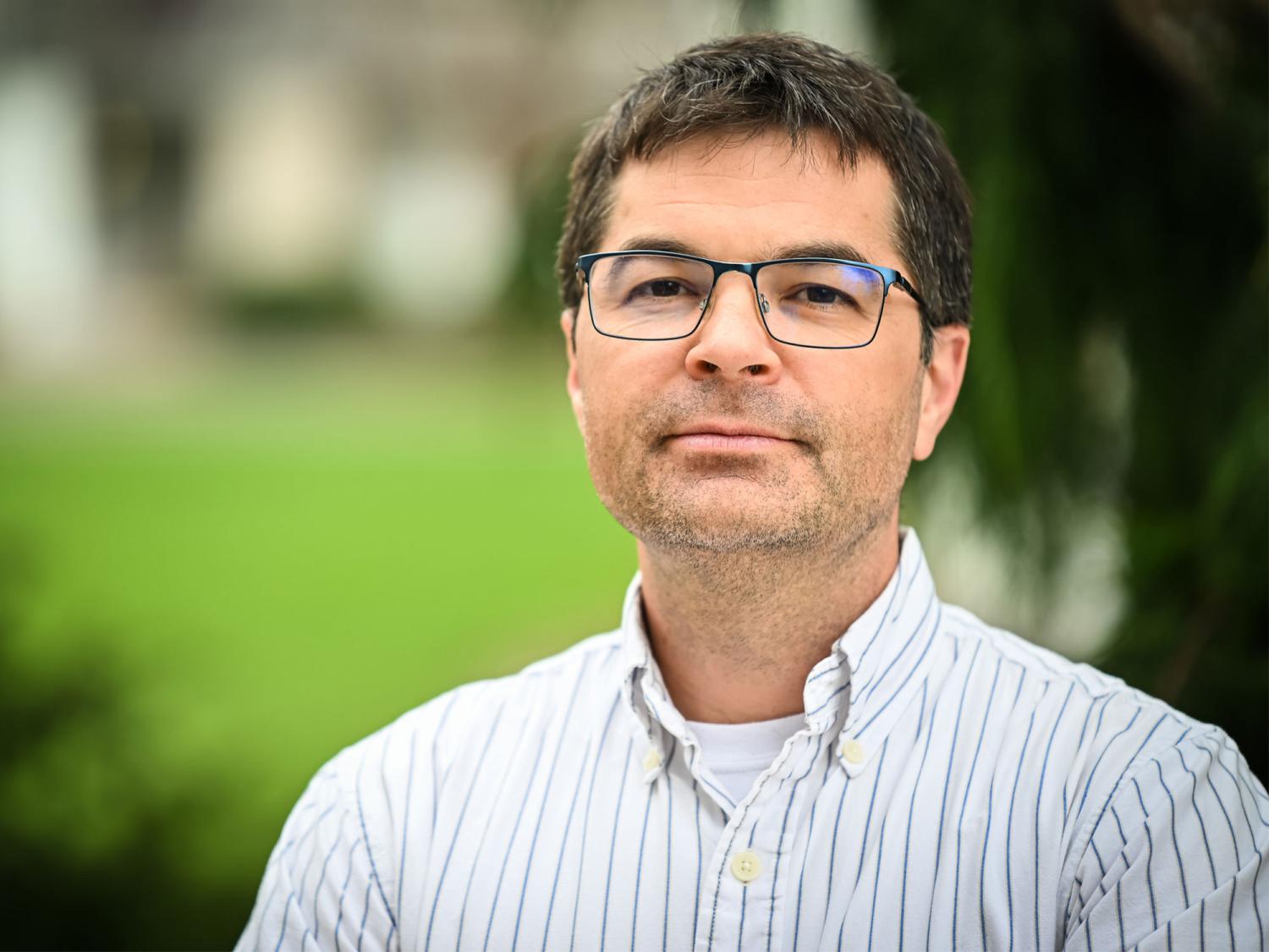 A photo of lead researcher Nathaniel Warner looking sternly at the camera in front of greenery