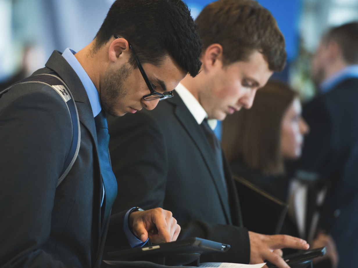 Students in business attire looking down at tech device