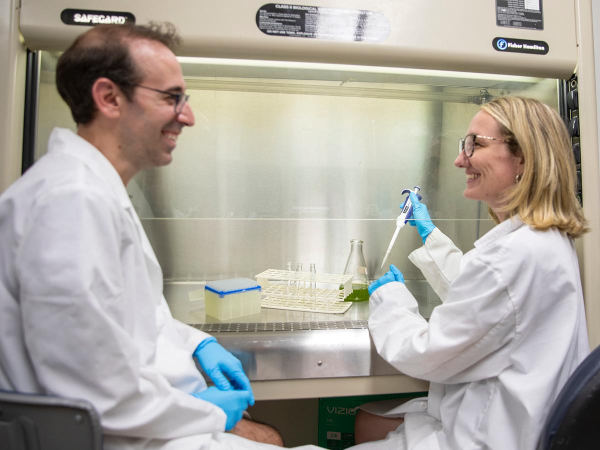 Two scientists wearing lab coats test lake water under an organic chemistry ventilation hood