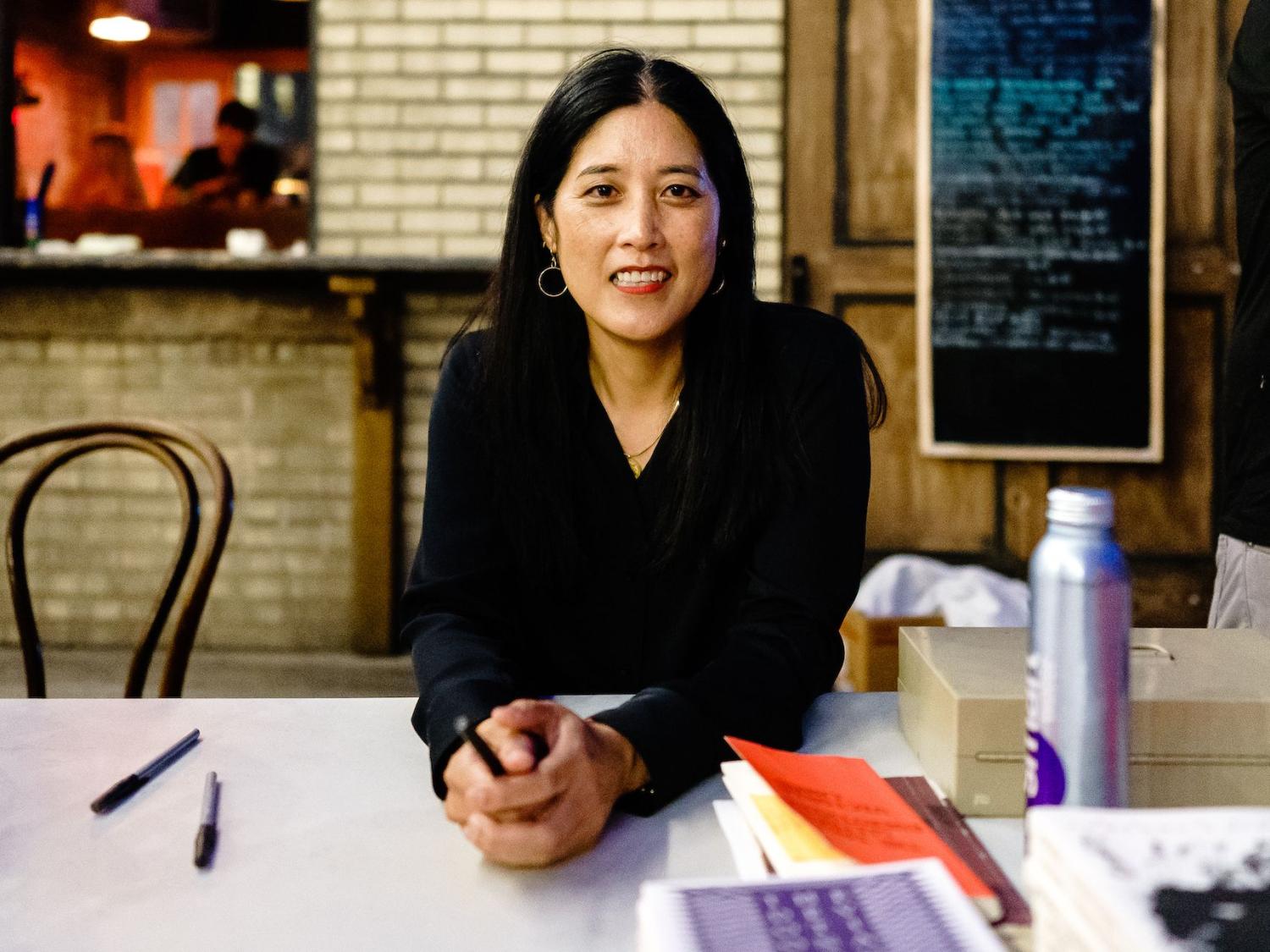 Poet Victoria Chang seated at a resaurant table with chalkboard menu and kitchen in background 