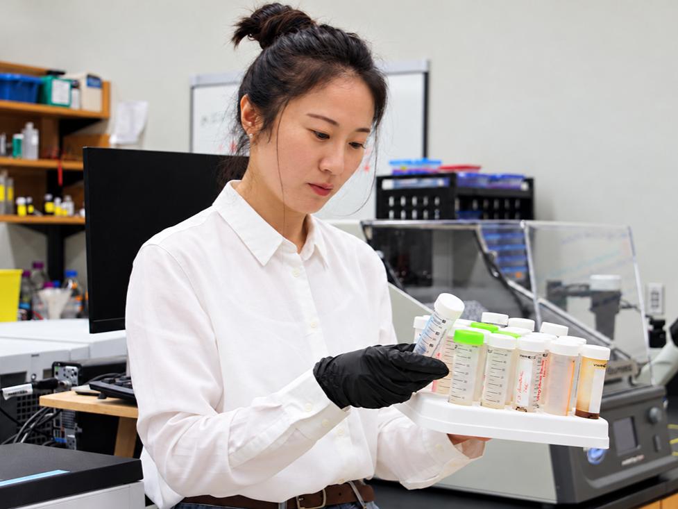 Researcher in a lab holding a rack of tubes. 