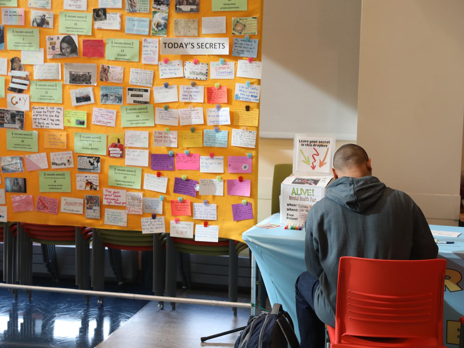 Student writing notecard for "Share a Secret" wall display