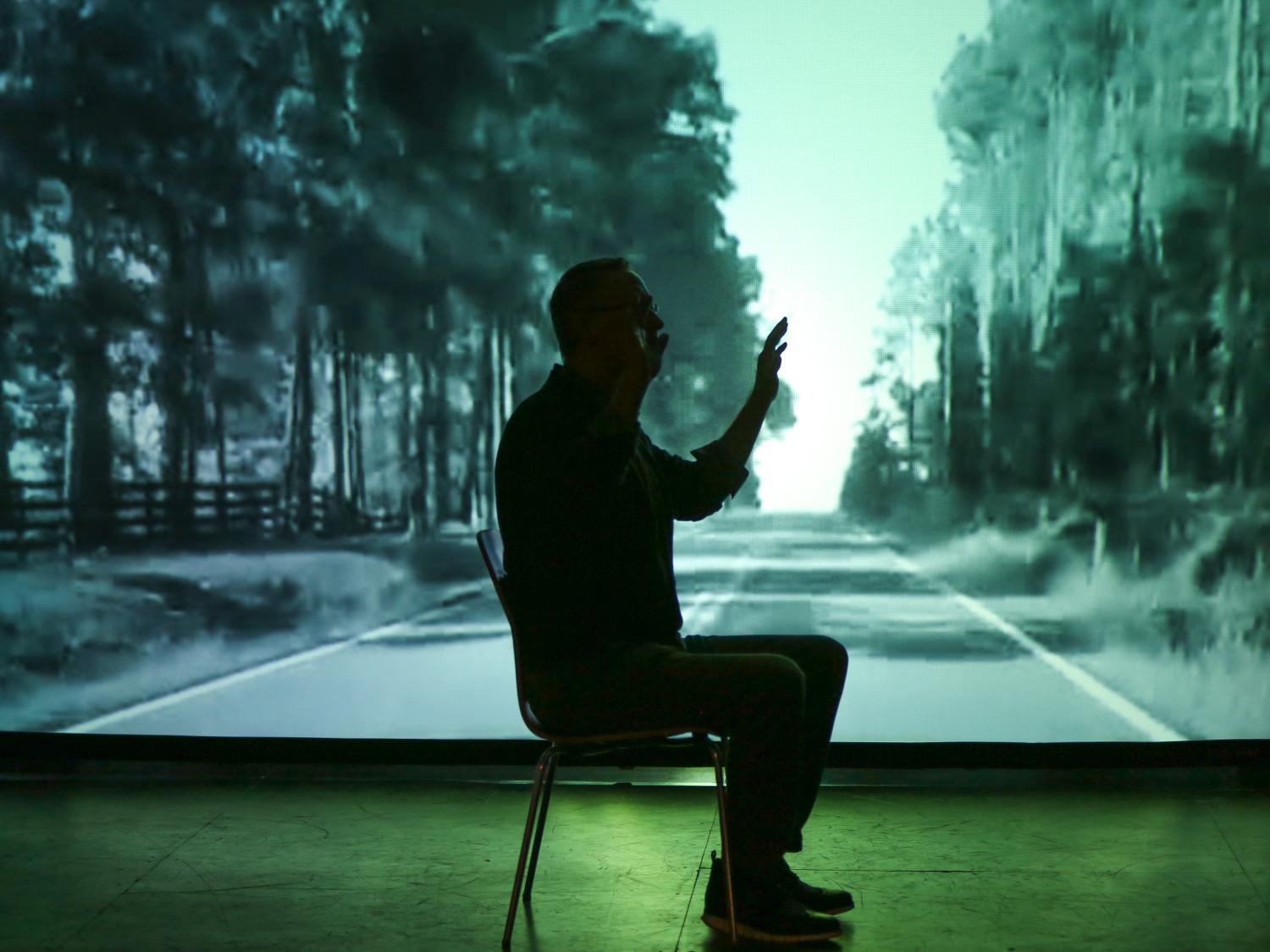 Bill Doan sits in shadow in front of the screen during rehearsal for "Drifting." 