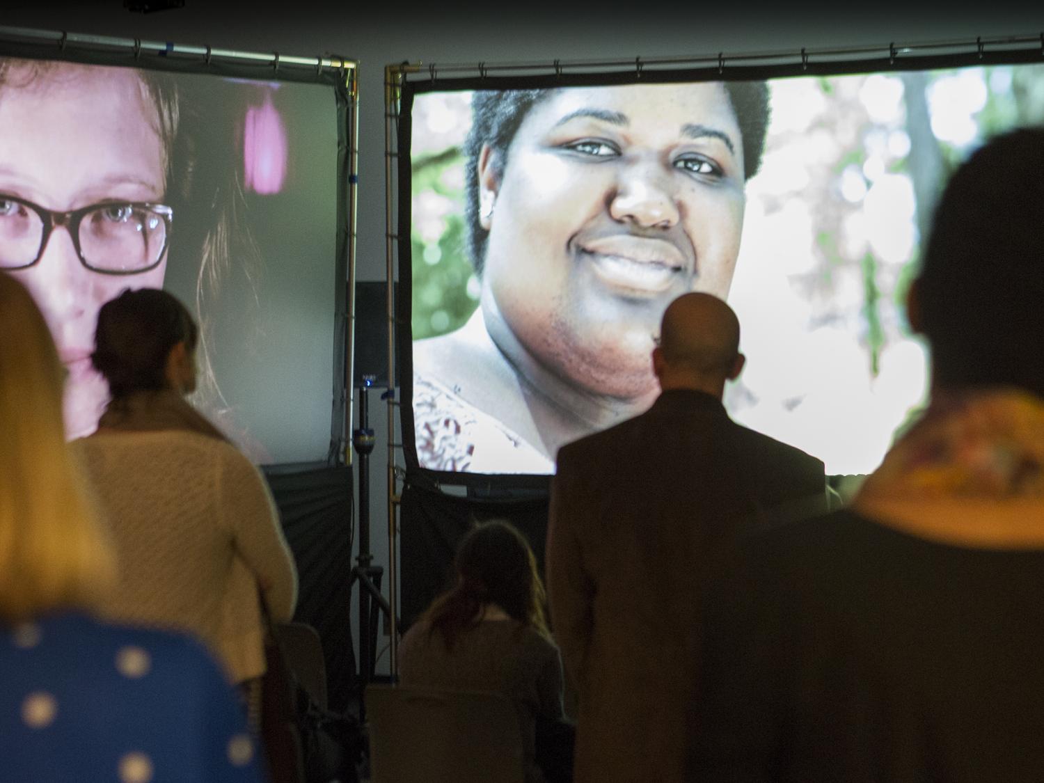 Audience members look at three large television screens