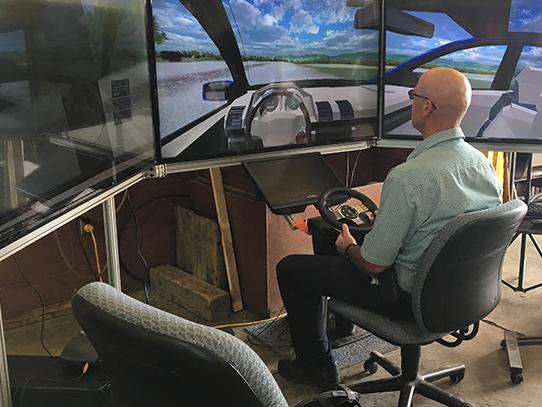 Man sitting in front of a three screen driving simulator.