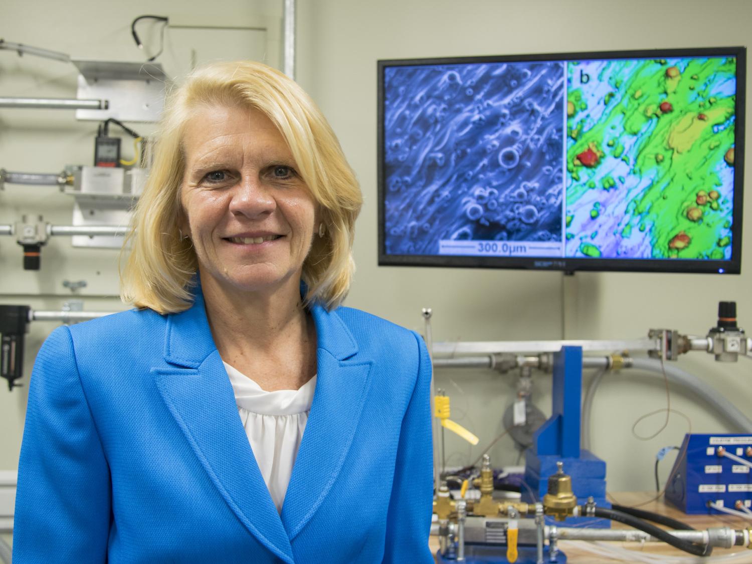 A female engineering professor stands in front of screens and machinery.
