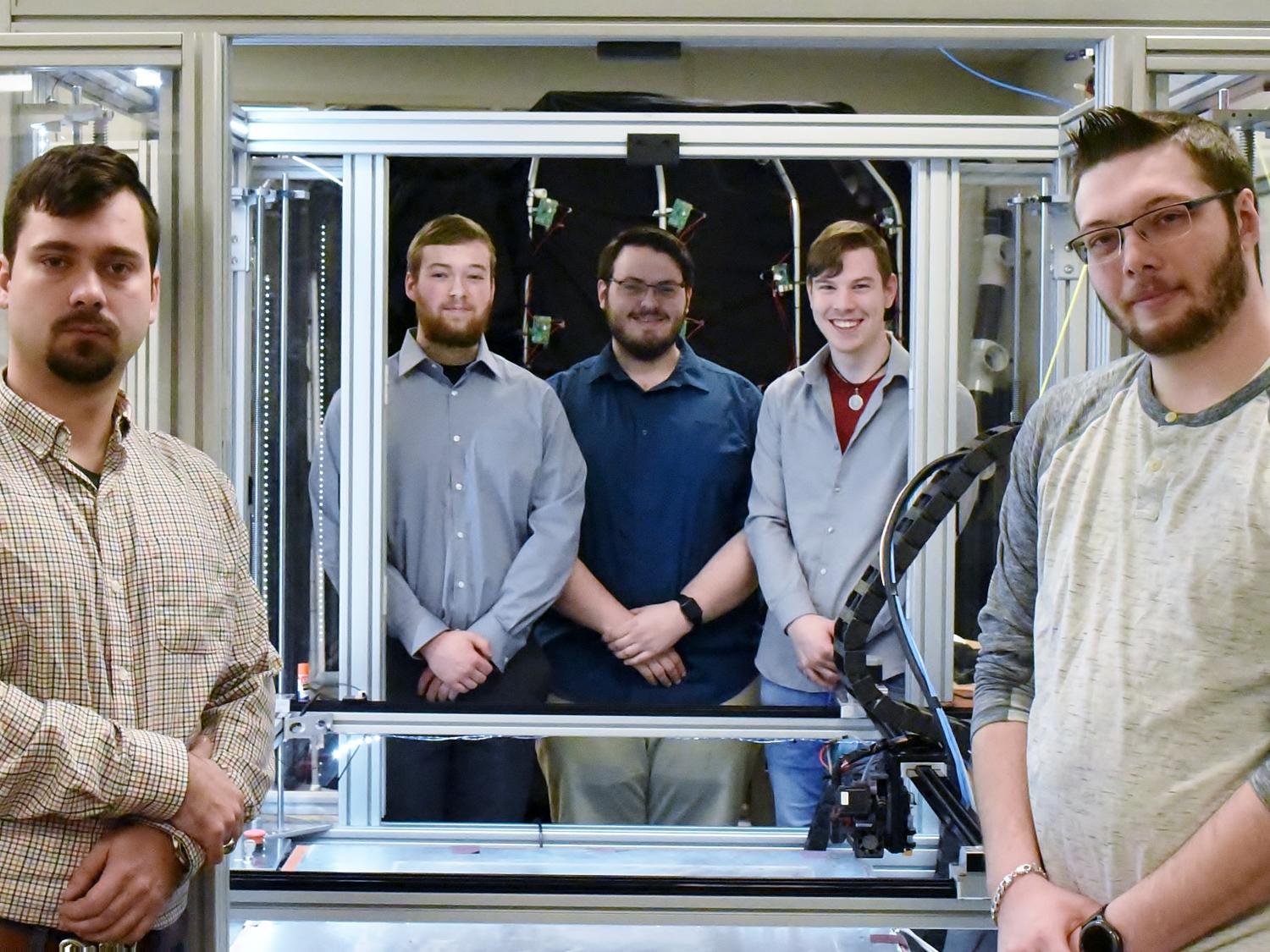 Five students pose near a large-scale 3D printer in Penn State Behrend's Innovation Commons lab.