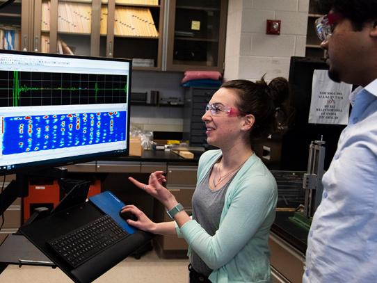 Two researchers examine an ultasonic wave readout on a computer monitor.
