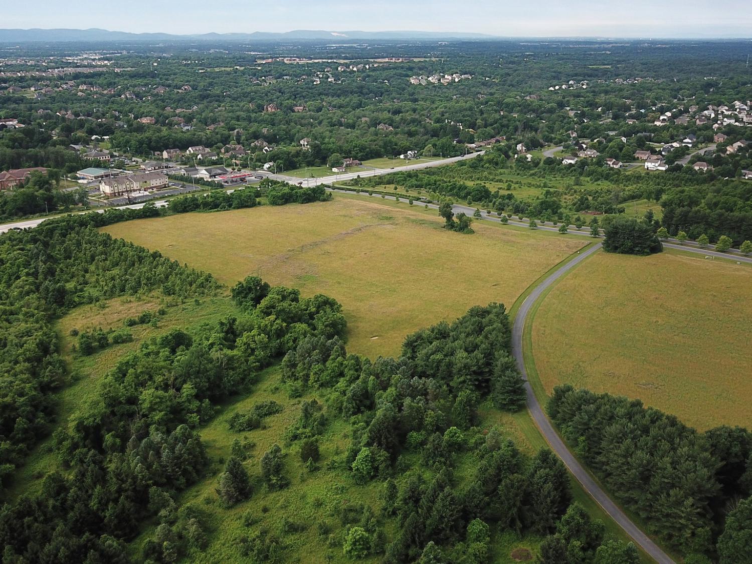 An aerial view of a plot of land. Several trees are in the foreground, while various businesses and homes are visible in the distant background.