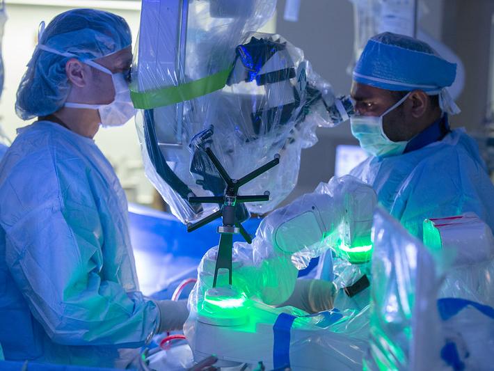 Two people dressed in surgical scrubs look into a robot while performing surgery.