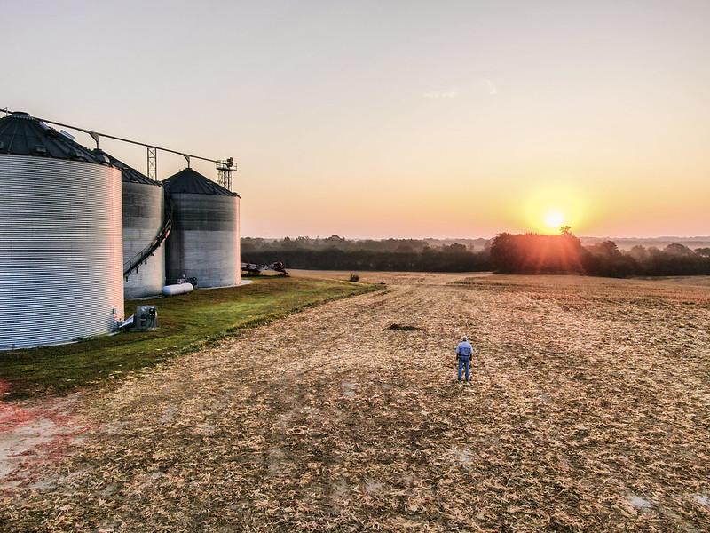 Grain storage and farm land against a setting sun