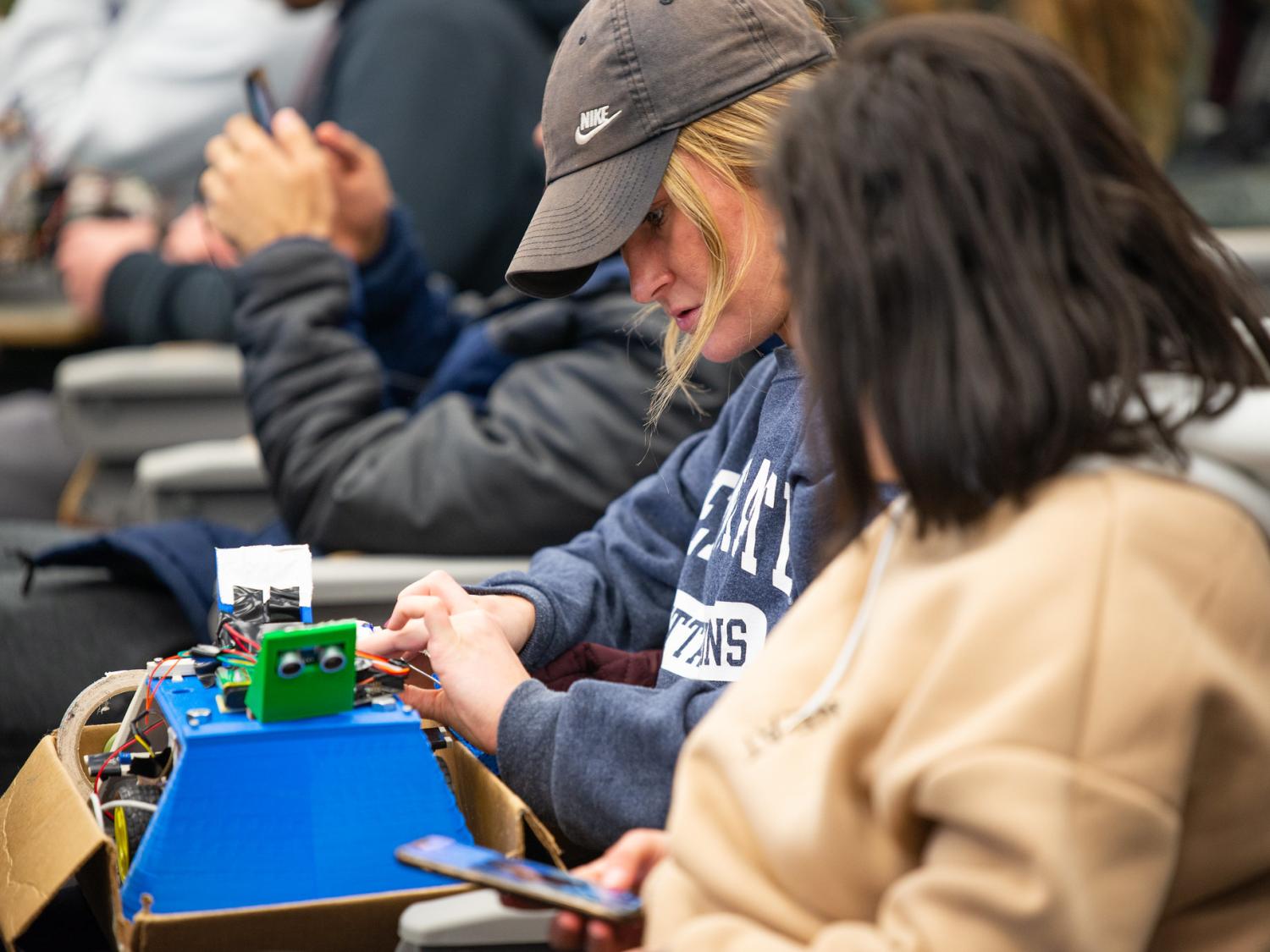 A female student adjusts a custom built robot in a classroom setting. 