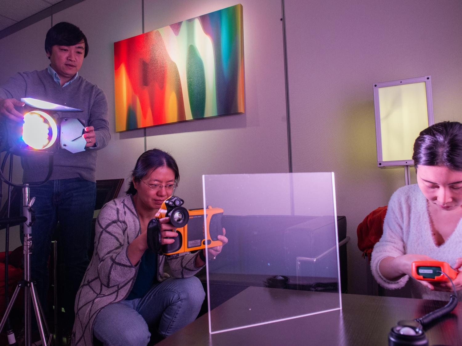 A man positions a light as two women take measurements on a pane of glass.
