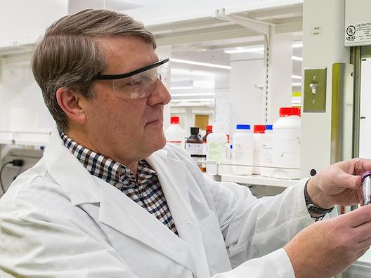 Man in lab coat looking at vial of bio-oil. 