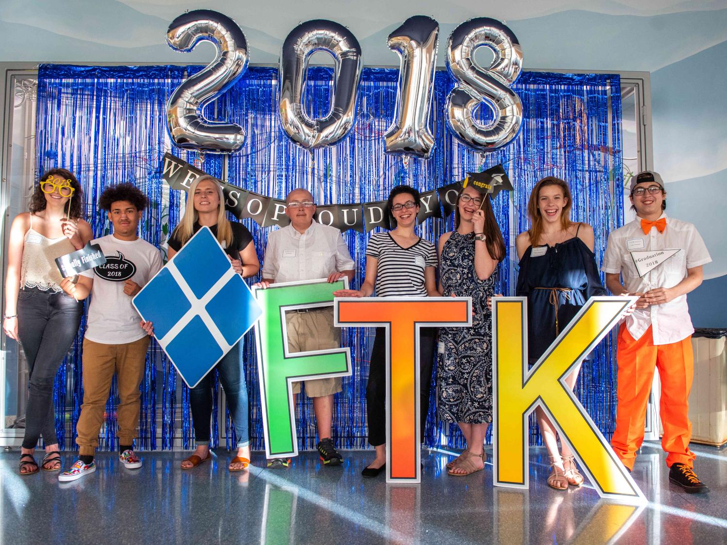 Eight people pose for a photo holding oversized letters “F-T-K” and a Four Diamonds logo. Balloons spelling out “2018” are above their heads.