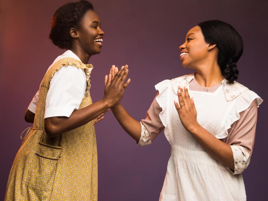 Two women smile at each other while they play a hand-clapping game.