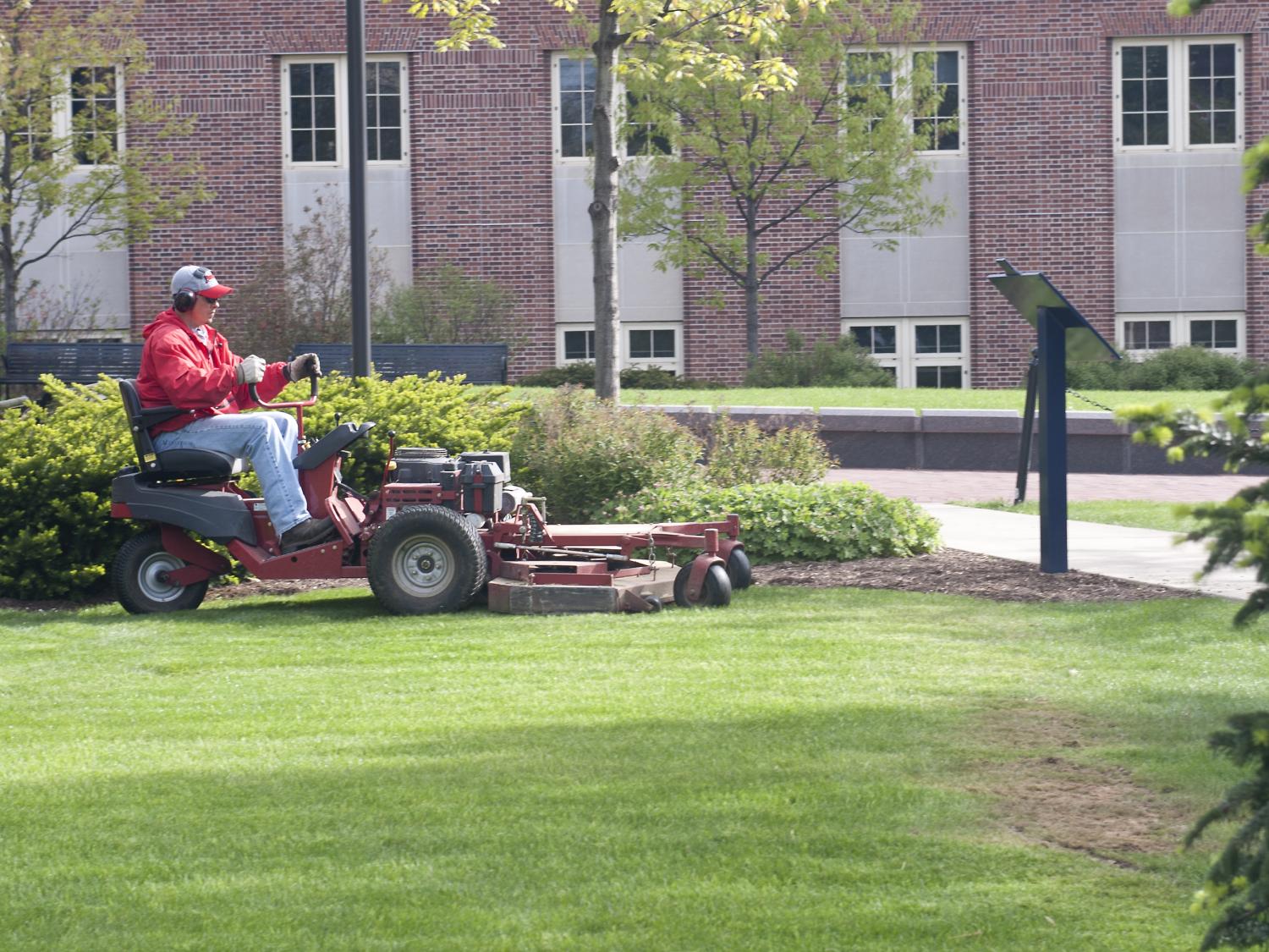 A man mowing grass on campus