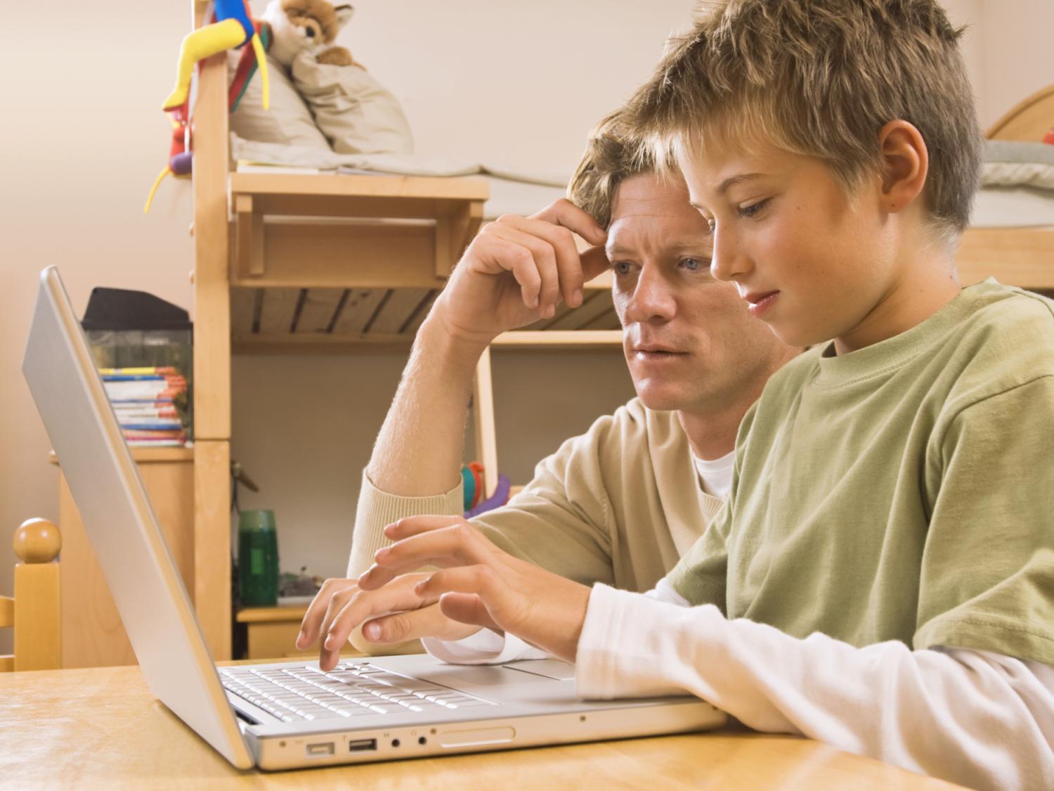 a father looking at a laptop screen with his son at the keyboard