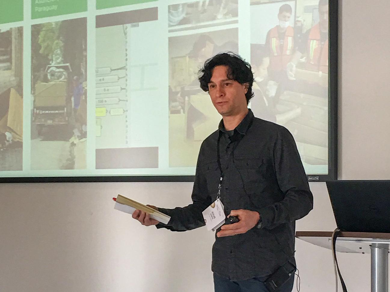 Julio Diarte, at right, motions to a screen onto which his work is displaying during a presentation.