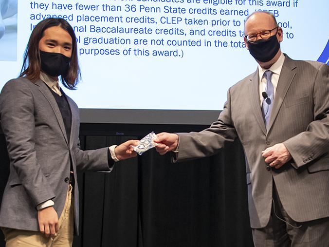 Two men in suits wearing face masks pose for a photo while the man on the right, Chancellor Patrick M. Jones, hands an award to student Pingxu Hao, left.
