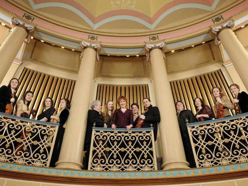 The musicians of Apollo's Fire stand on a balcony and look down to the photographer.