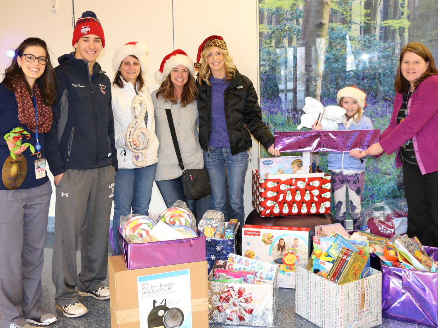 Seven people pose for a photo. In front of them are several boxes of gifts.