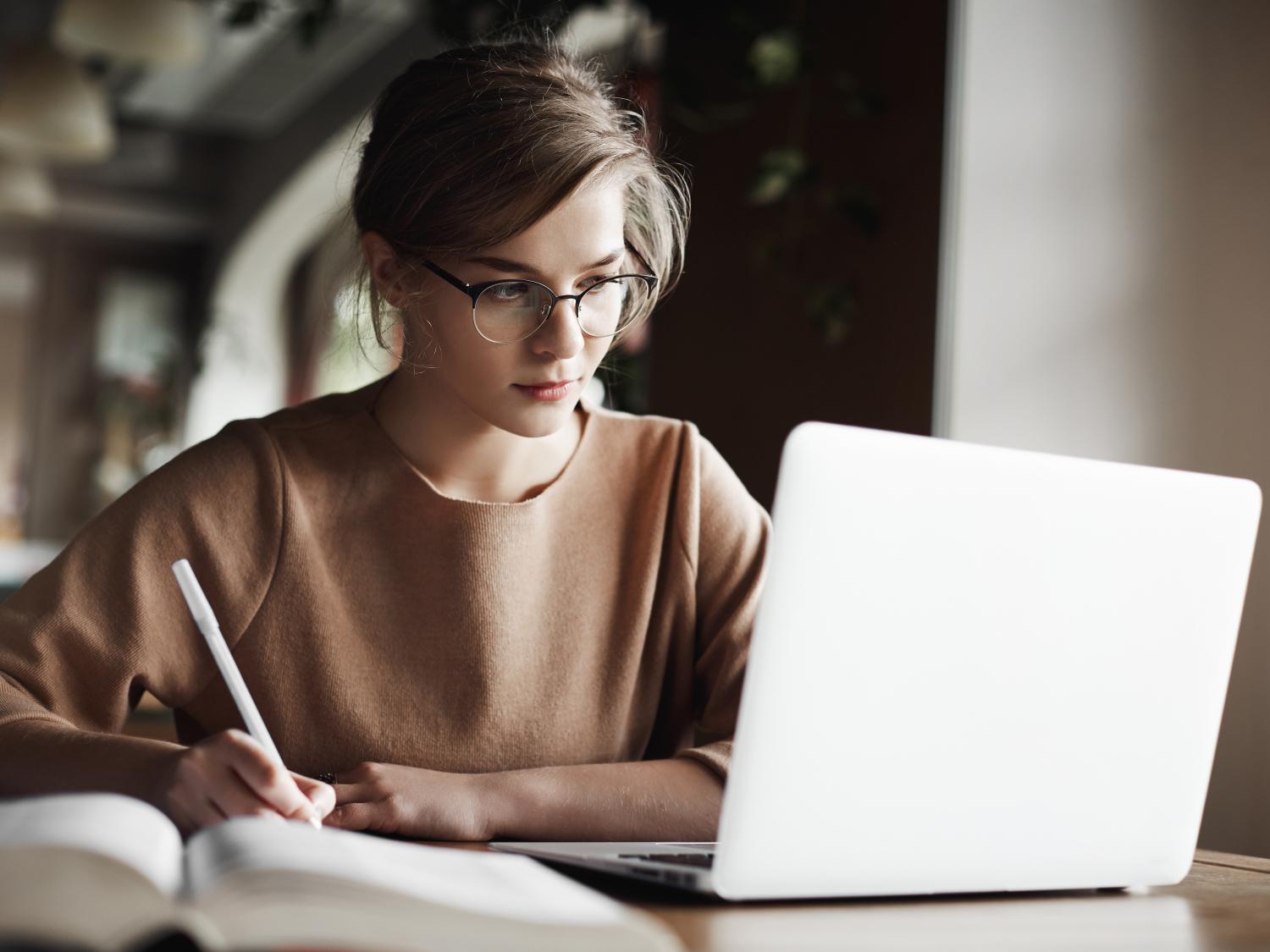 Young woman with sweatshirt and glasses works on her computer
