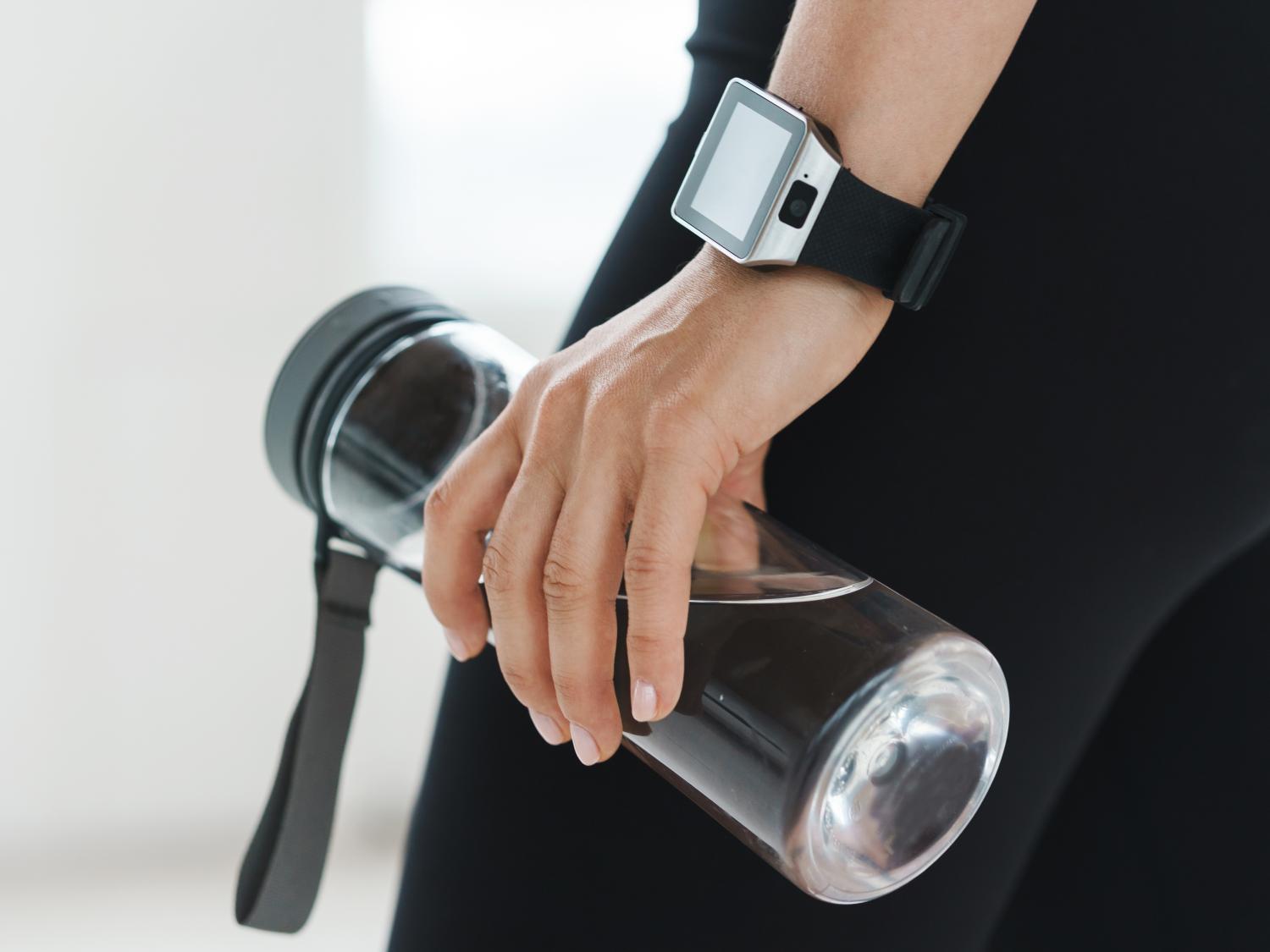 A hand wearing a Smartwatch and holding a water bottle