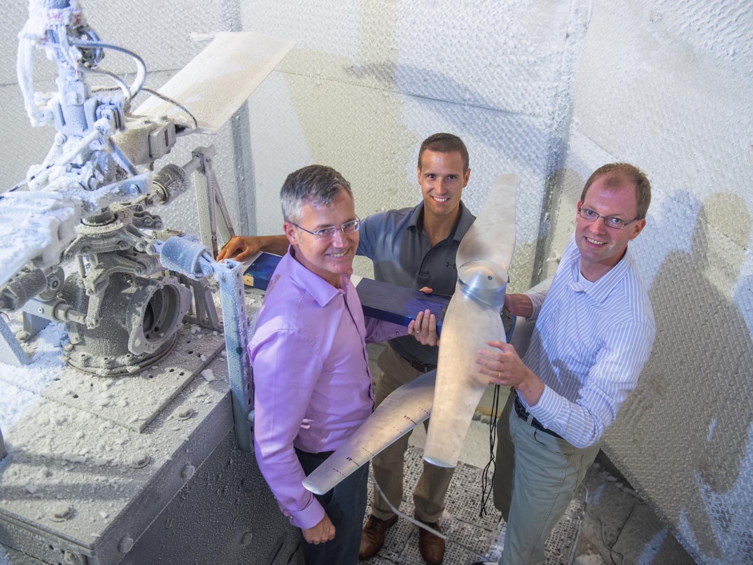 Three men stand in a steel chamber, around a steel blade and next to a larger rotor. The rotor and the walls of the chamber are covered in ice. 