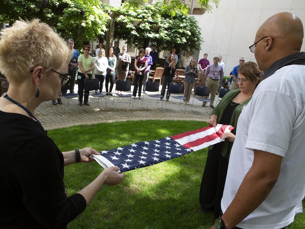 Two women fold the American flag. A crowd of people watch from a distance.