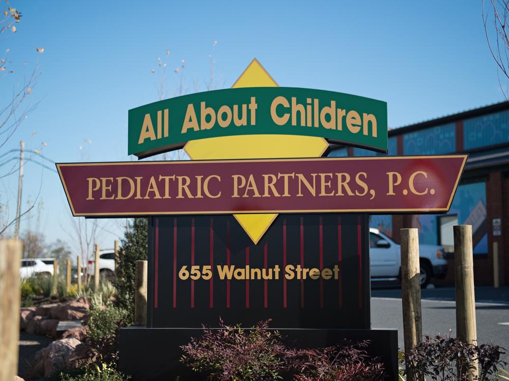 A sign that says, "All About Children Pediatric Partners, LLC," in front of a brick building.