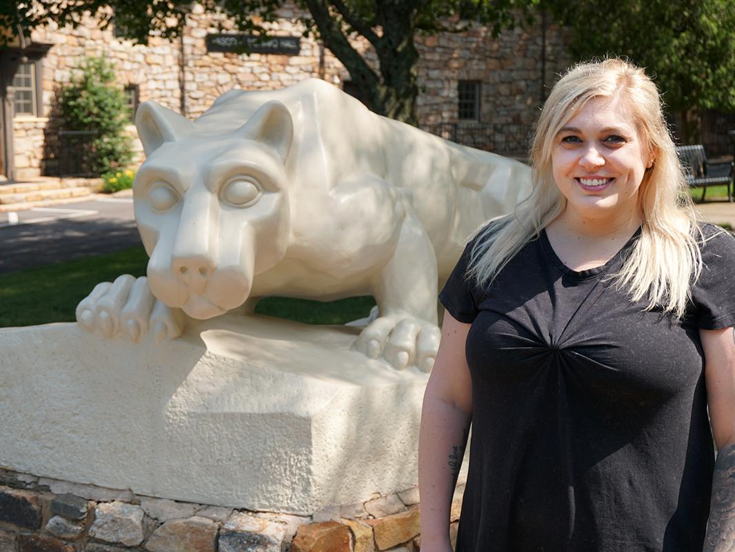 Woman in black dress standing next to statue of Nittany Lion on Penn State Hazleton campus.