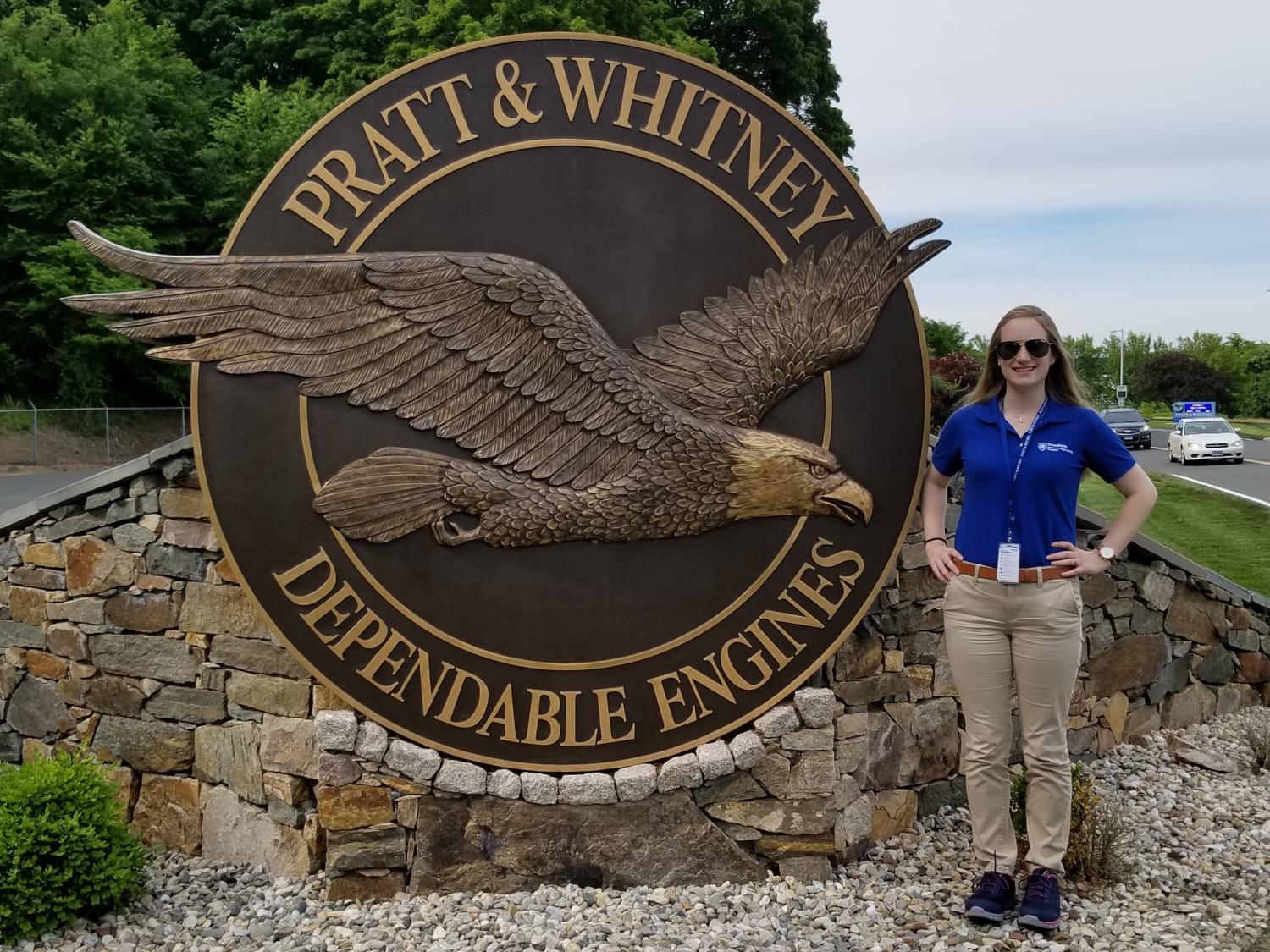 A female undergraduate student poses next to a sign with the Pratt & Whitney logo. 