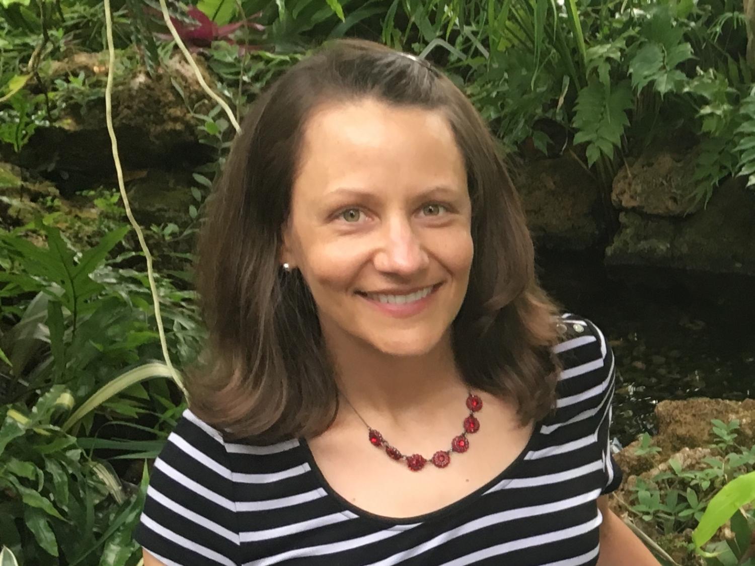 Brunette woman posing in front of shrubbery.