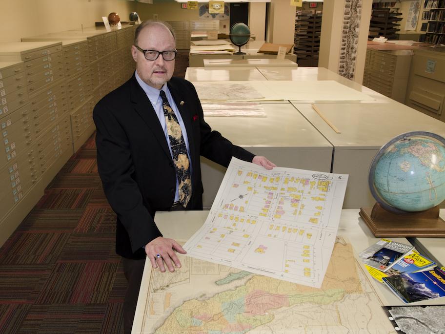 man standing in Maps Library holding maps